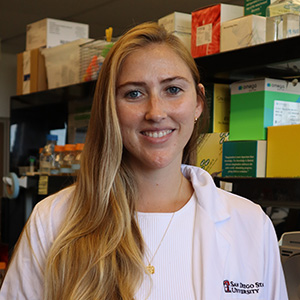 Headshot of Morgan Farrell wearing lab coat in front of shelves in the lab
